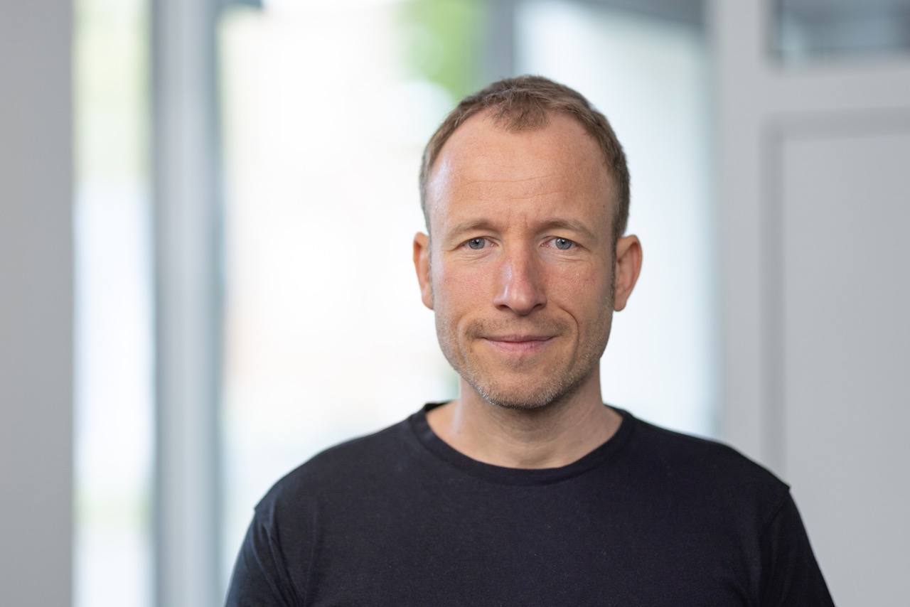 Zu sehen ist Danilo Ziemen in einem schwarzen T-Shirt vor einem weißen Hintergrund.